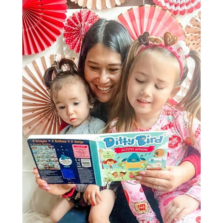 Ditty Bird Sound Book Action Songs USB-C Rechargeable; mother and two kids read it together amid festive decor.