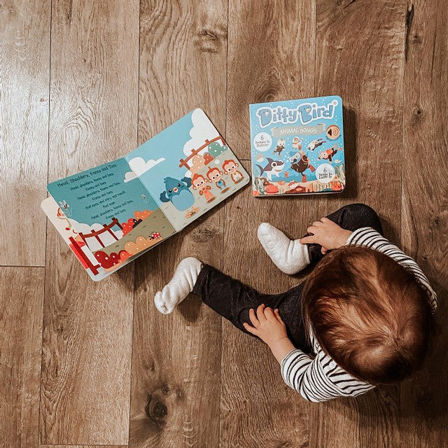 Ditty Bird Sound Book Animal Songs USB-C Rechargeable; child sits on a wooden floor beside the blue animal book.
