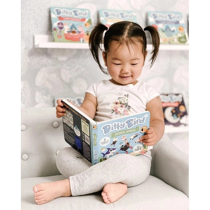 Ditty Bird Sound Book Animal Songs USB-C Rechargeable; toddler sits on a sofa reading the colorful book.