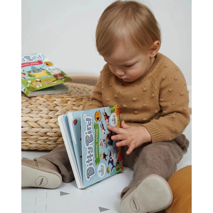 Ditty Bird Sound Book Animal Songs USB-C Rechargeable held by a toddler turning colorful animal pages.