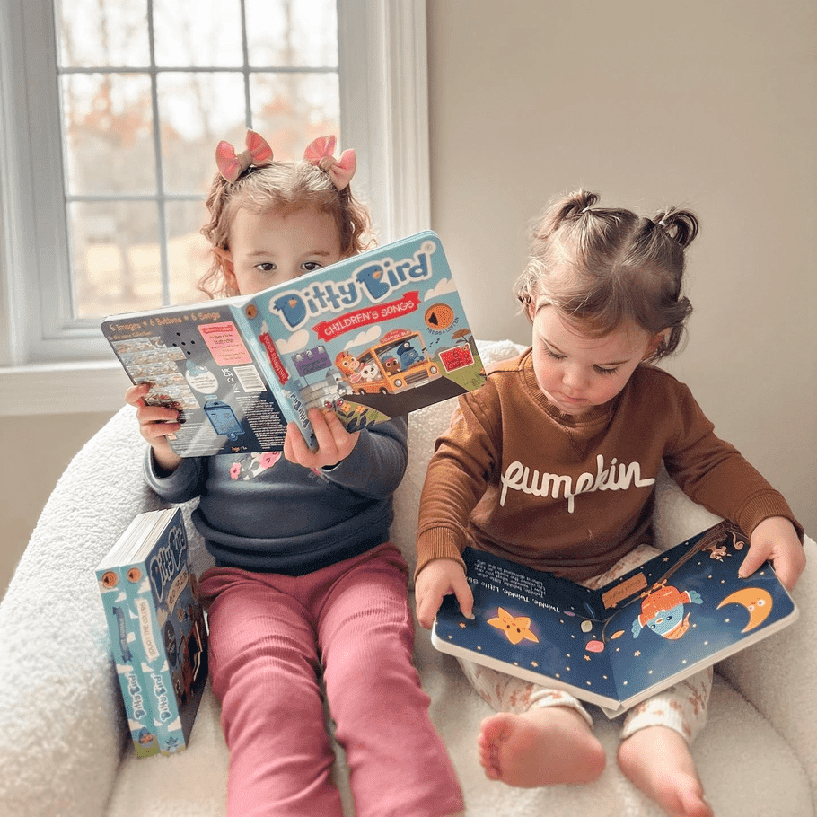 Ditty Bird Sound Book: Children's Songs USB-C Rechargeable; two kids cozy on a sofa reading the colorful book.