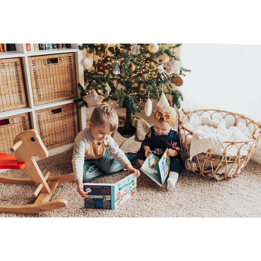 Ditty Bird Sound Book Christmas Songs USB-C Rechargeable for kids, two toddlers read beside a lit Christmas tree.