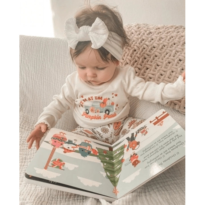 Ditty Bird Sound Book Christmas Songs USB-C Rechargeable being read by a baby on a cozy sofa, festive moment.