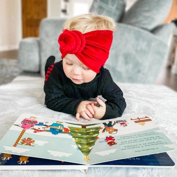 Ditty Bird Sound Book Christmas Songs USB-C Rechargeable, toddler turning pages with a red headband.