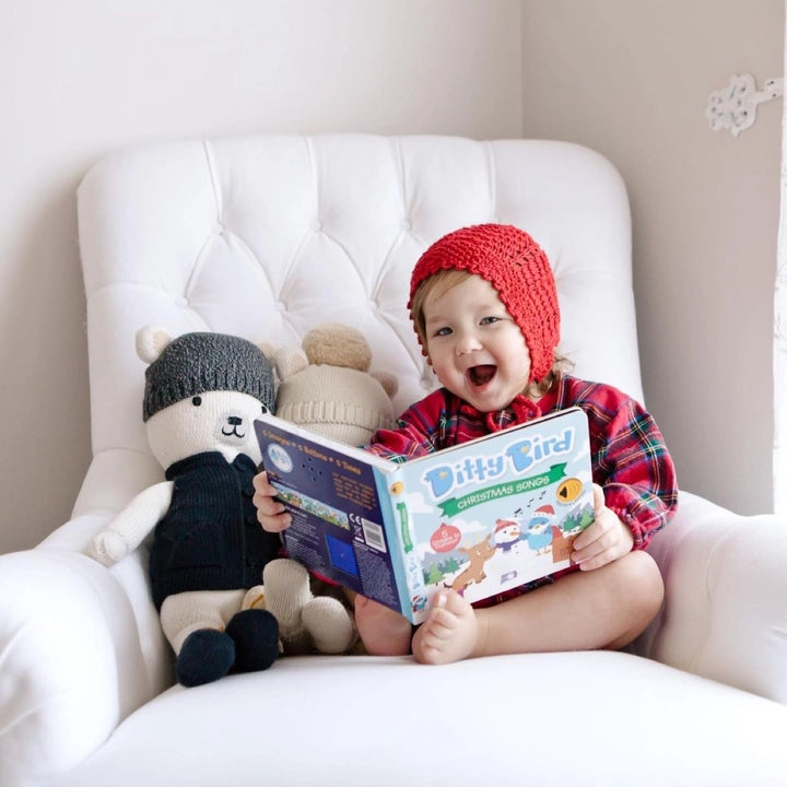 Ditty Bird Sound Book Christmas Songs USB-C Rechargeable; smiling baby reads it on a white chair with plush bears.