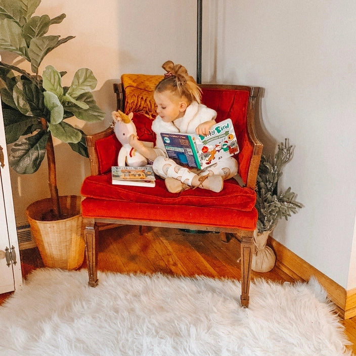 Ditty Bird Sound Book Christmas Songs USB-C Rechargeable; child sits on red velvet chair reading the book beside a plush unicorn.