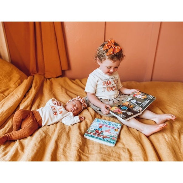 Ditty Bird Sound Book Classical Ballet Music USB-C Rechargeable read by an older child on an orange bed, with a sleeping baby nearby.