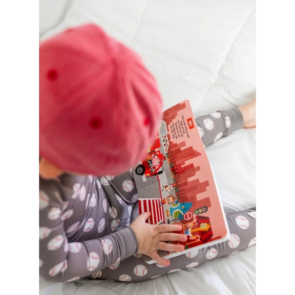 Ditty Bird Sound Book Color Songs USB-C Rechargeable; a child sits on a bed reading the colorful cityscape book.