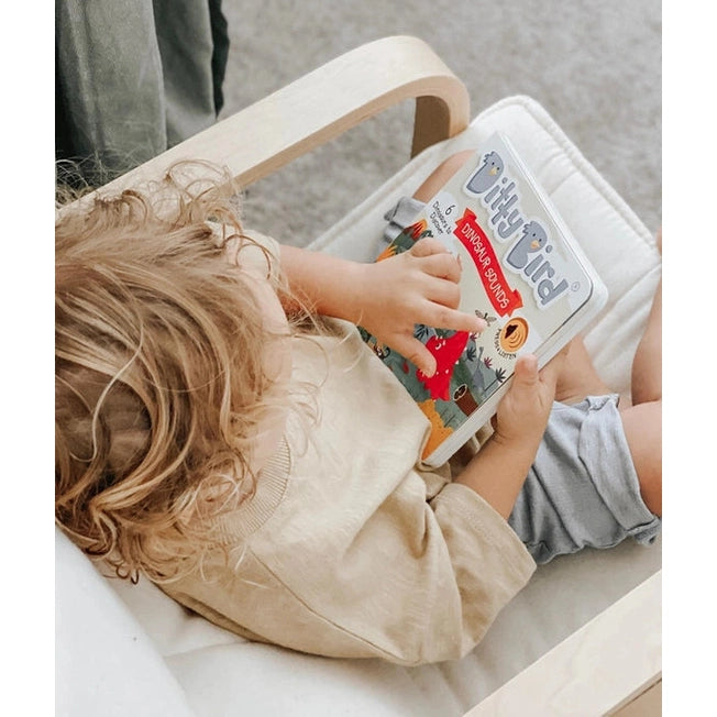 Ditty Bird Sound Book Dinosaur Sounds USB-C Rechargeable, a toddler reads it on a wooden chair.