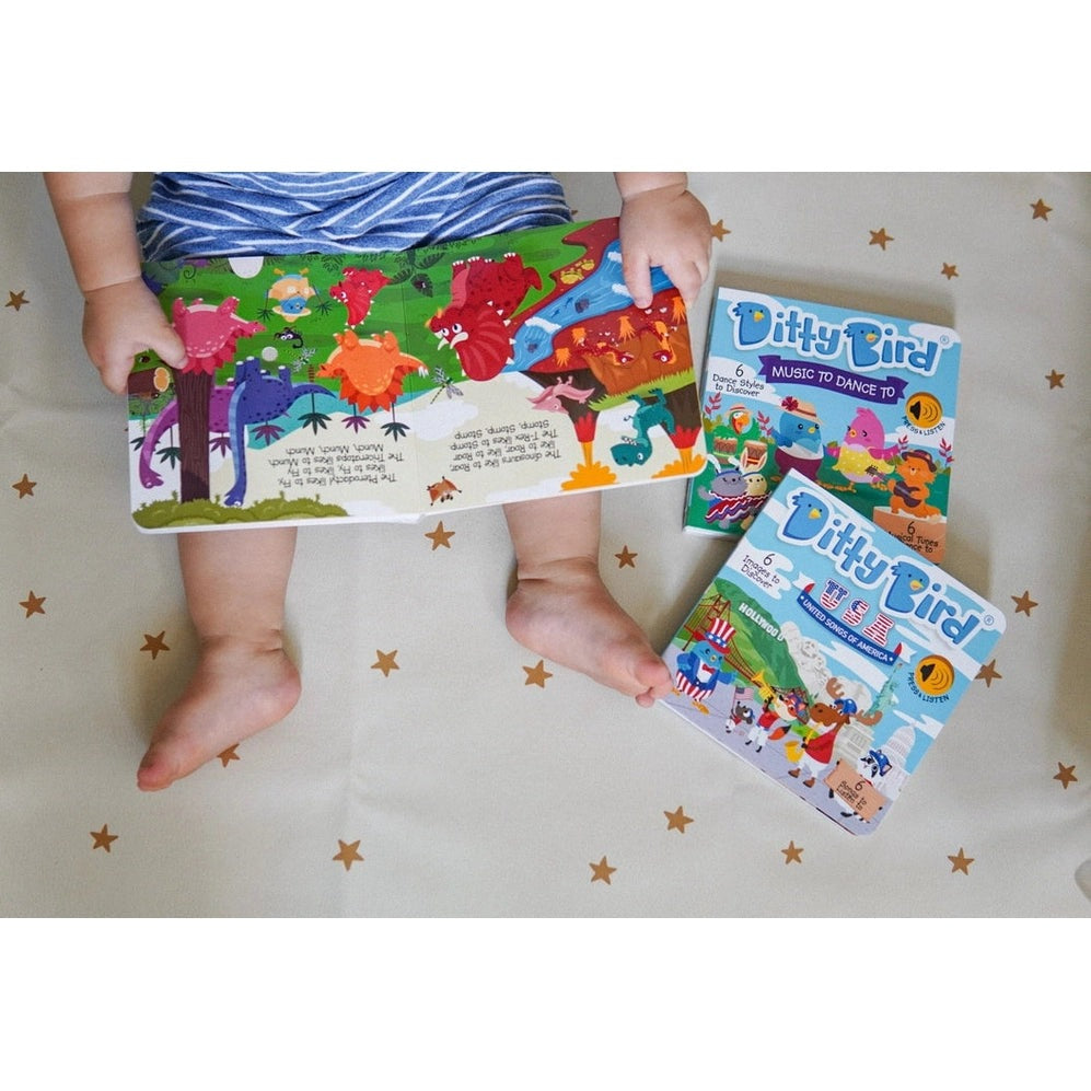 Ditty Bird Sound Book Dinosaur Sounds USB-C Rechargeable held by a toddler on a starry bedspread, with colorful dinosaur pages.