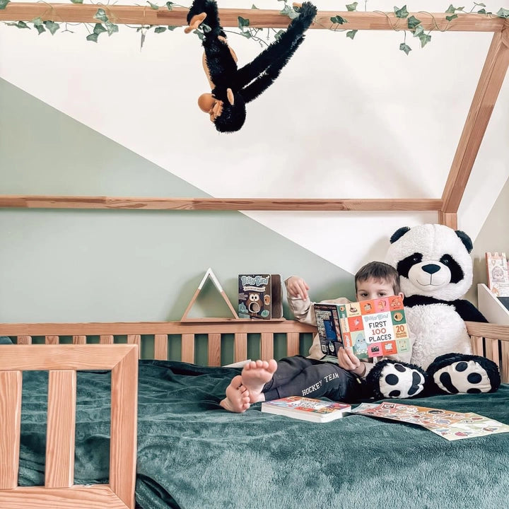 Child lounges on a bed with a panda plush, reading Ditty Bird Sound Book First 100 Places USB-C Rechargeable.