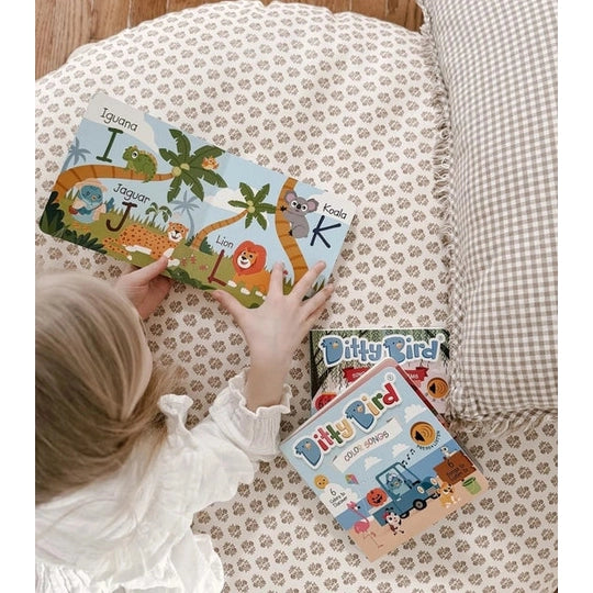 Ditty Bird Sound Book Fun Alphabet USB-C Rechargeable; child sits on a patterned bed, holding the colorful animal alphabet card.