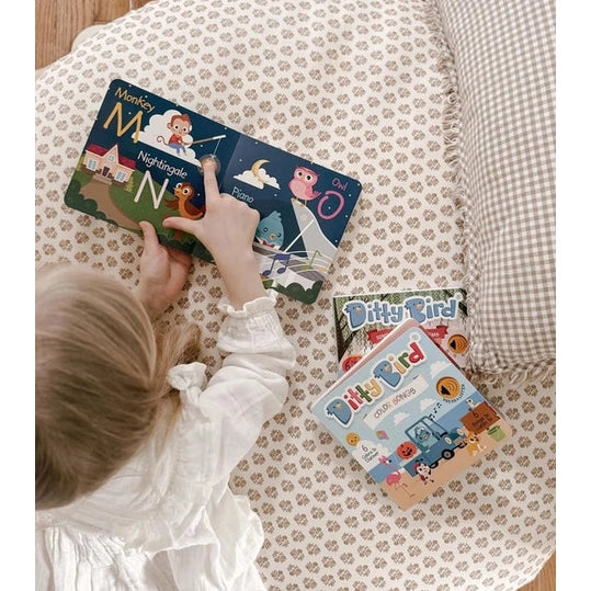 Ditty Bird Sound Book Fun Alphabet USB-C Rechargeable; a toddler explores colorful pages on a cozy patterned bedspread.
