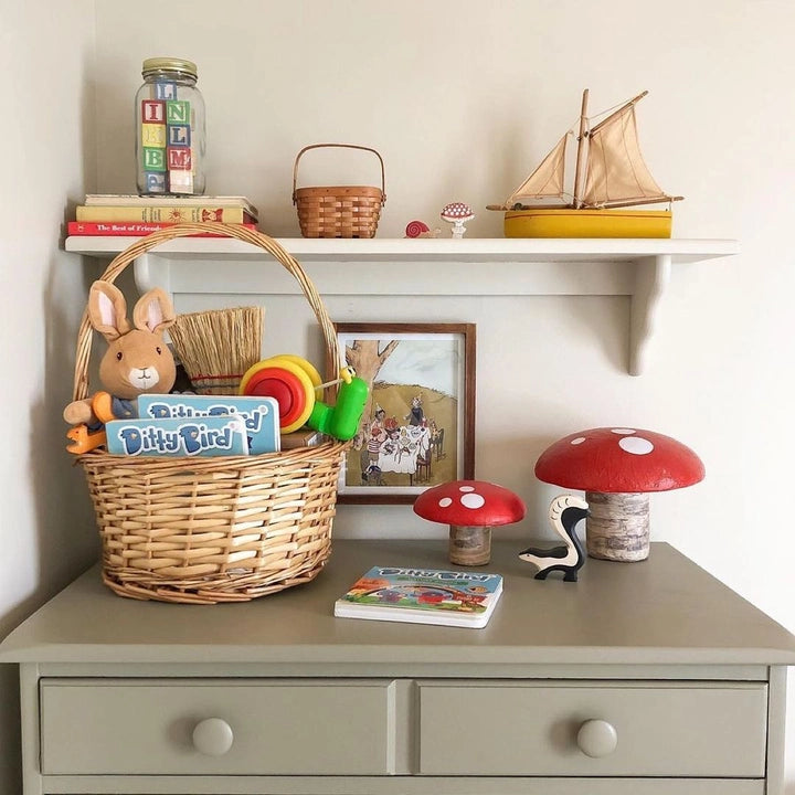 Ditty Bird Sound Book Funny Songs USB-C Rechargeable in a wicker basket with plush bird and colorful toys on a dresser.