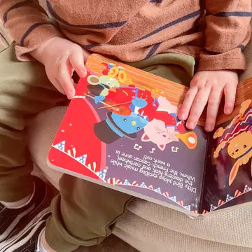 Ditty Bird Sound Book Music to dance to USB-C rechargeable, held open by a toddler to reveal colorful illustrated pages.