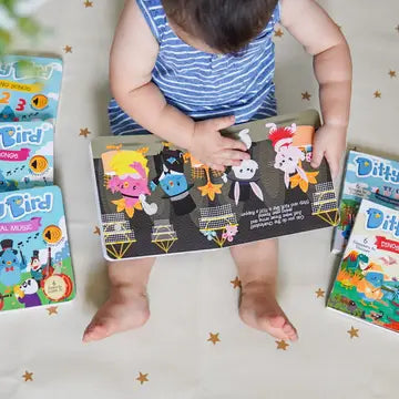 Ditty Bird Sound Book Music to Dance To USB-C Rechargeable; a baby sits barefoot reading the colorful open book.