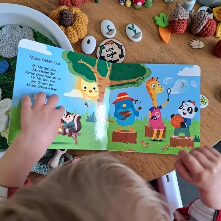 Ditty Bird Sound Book Nature Songs USB-C Rechargeable; a toddler taps a colorful page with a cheerful animal band on display.