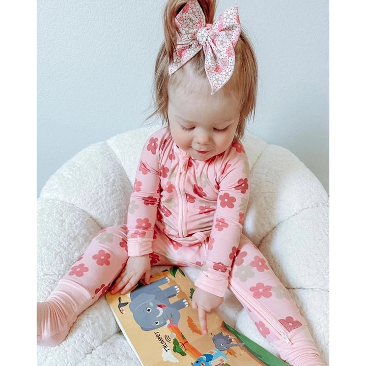 Ditty Bird Safari Animal Sounds USB-C Rechargeable educational toy; a baby in pink floral pajamas sits on a white chair, turning pages of the colorful sound book.