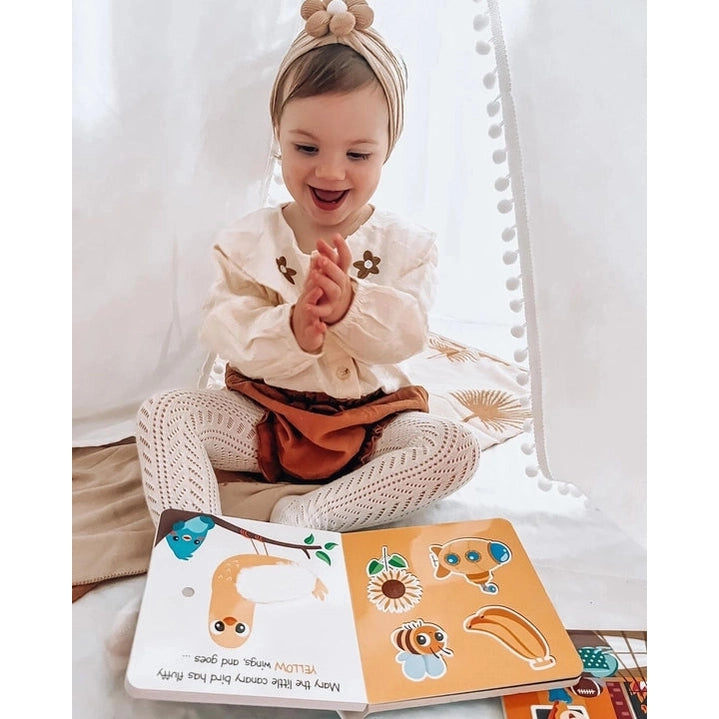 Ditty Bird Sound Book Touch the Colors USB-C Rechargeable, a smiling toddler clapping while reading colorful pages.