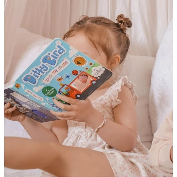Ditty Bird Sound Book Touch the Colors USB-C Rechargeable being read by a young girl on a sofa, showcasing interactive sounds.