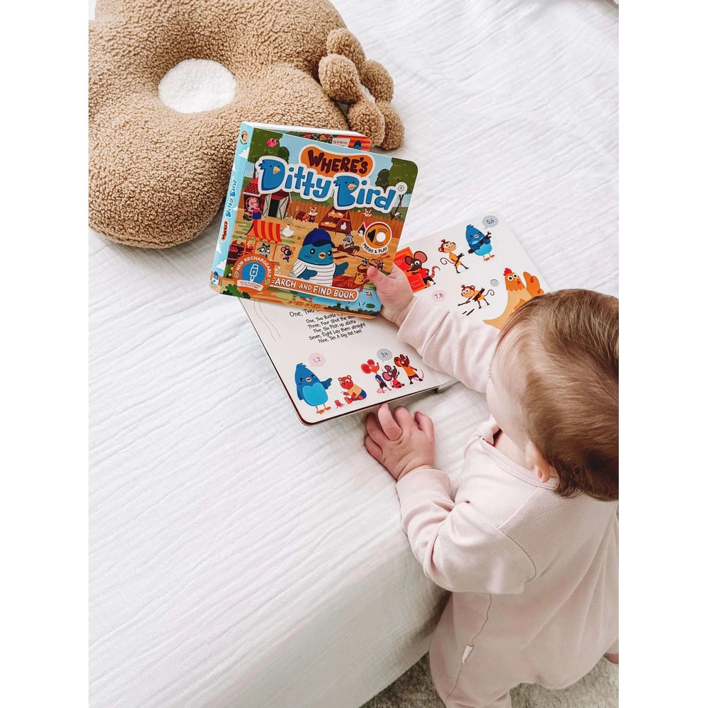 Ditty Bird Sound Book Where's Ditty Bird USB-C rechargeable; a baby explores the colorful pages on a white bed.