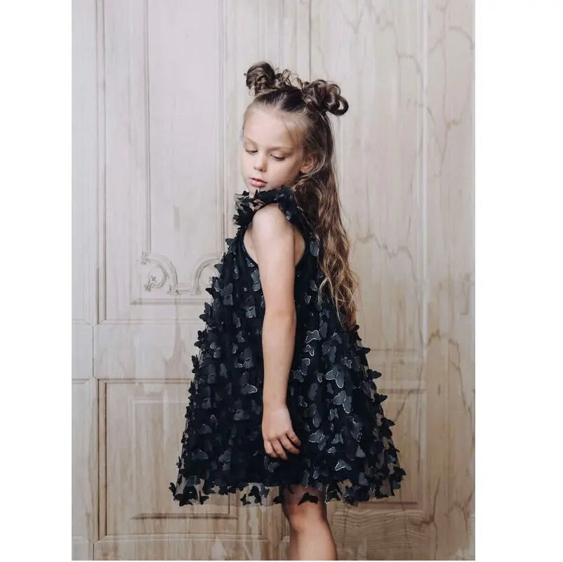 Dolly By Le Petit Tom Allover Butterflies Tutu Dress Black; toddler stands sideways to show 3D petal overlays.