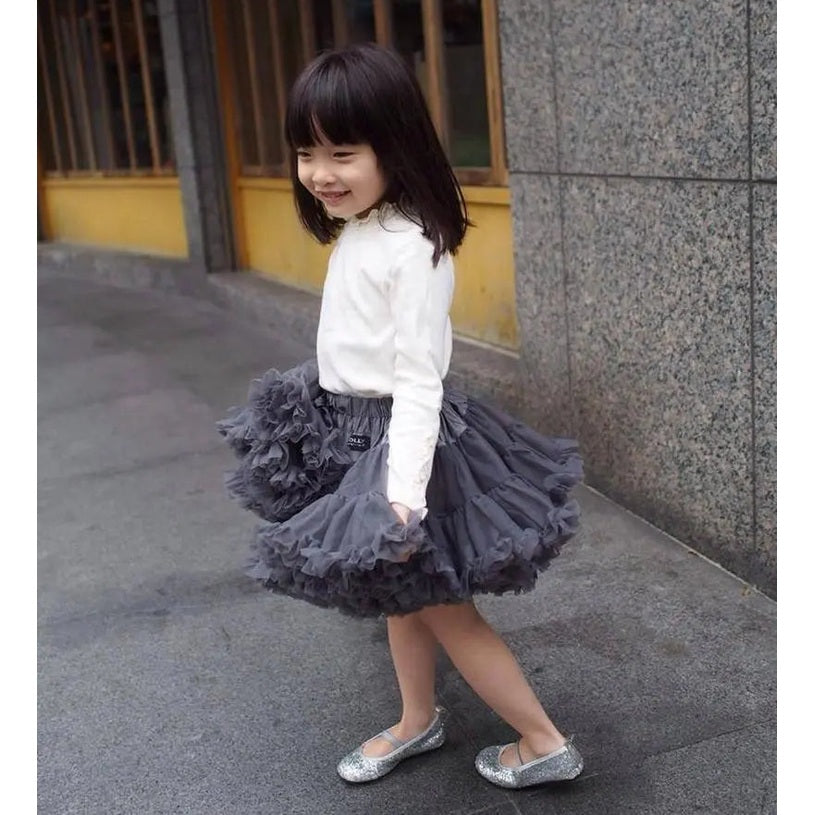 Dolly by Le Petit Tom Pettiskirt Princess & The Pea dark grey tulle skirt with layered ruffles, twirled by a smiling girl.