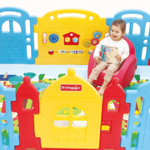 Dwinguler Castle Extension Set Rainbow play yard; child sits in a pink seat amid bright blue, yellow, and red castle panels.
