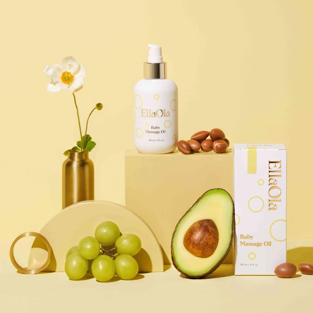 EllaOla Fragrance Free 100% USDA Organic Baby Massage Oil 150ml bottle sits beside a white box, avocado and grapes.