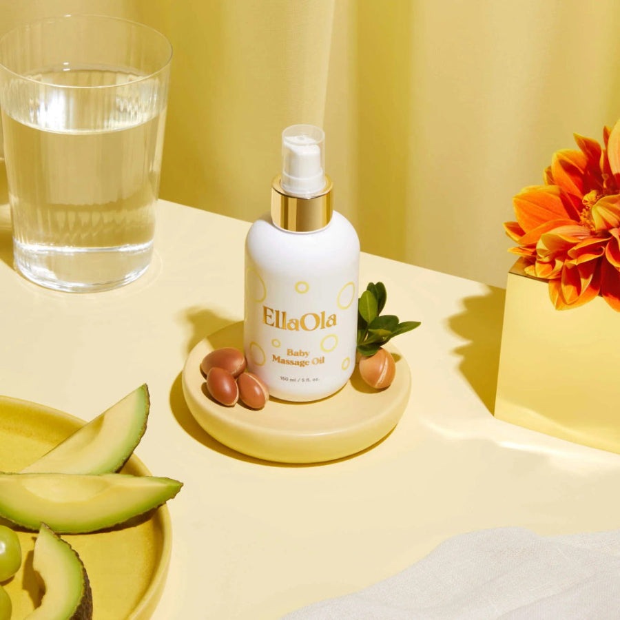 EllaOla Fragrance Free Baby Massage Oil bottle with pump sits on a yellow tray beside avocados.