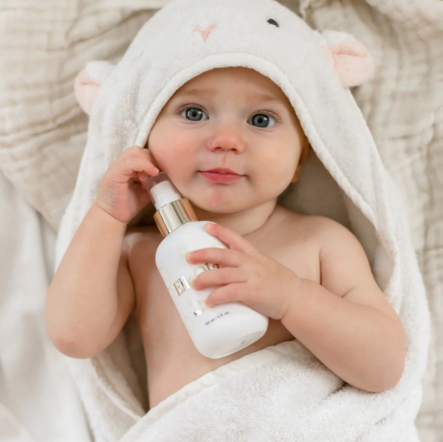 EllaOla Fragrance Free 100% USDA Organic Baby Massage Oil 150ml; baby in a white towel holds the bottle, touching cheek.