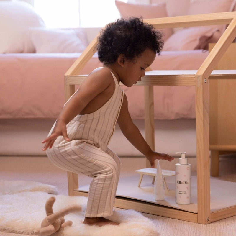 EllaOla Fragrance Free Hydrating Baby Lotion 230ml being reached for by a toddler under a wooden play structure.