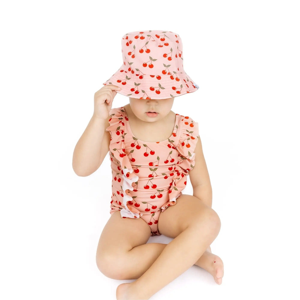 Child wearing a cherry-themed swimsuit and hat on a white background