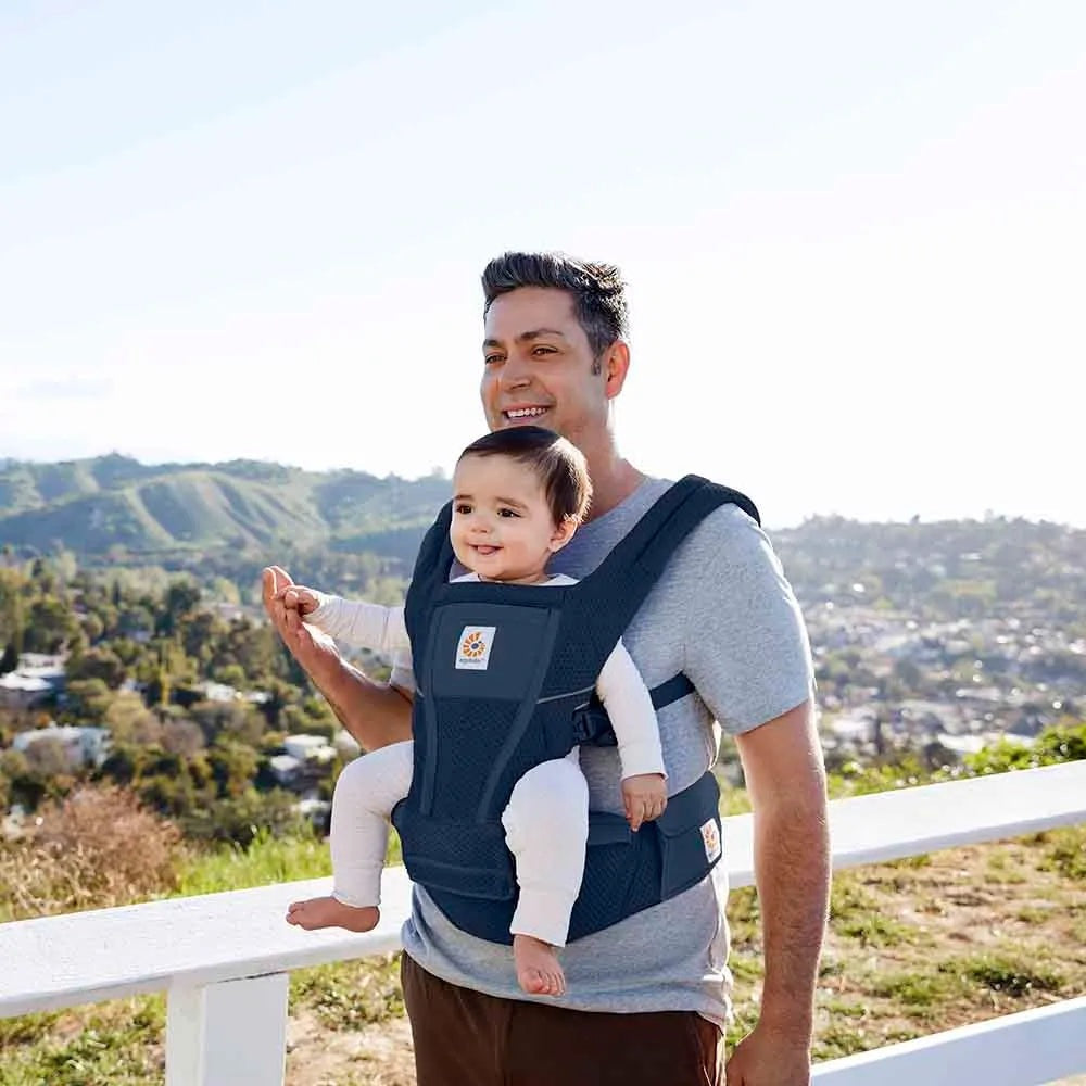 Ergobaby Alta Hip Seat Baby Carrier in dark blue, dad carries smiling infant on his hip with padded straps.
