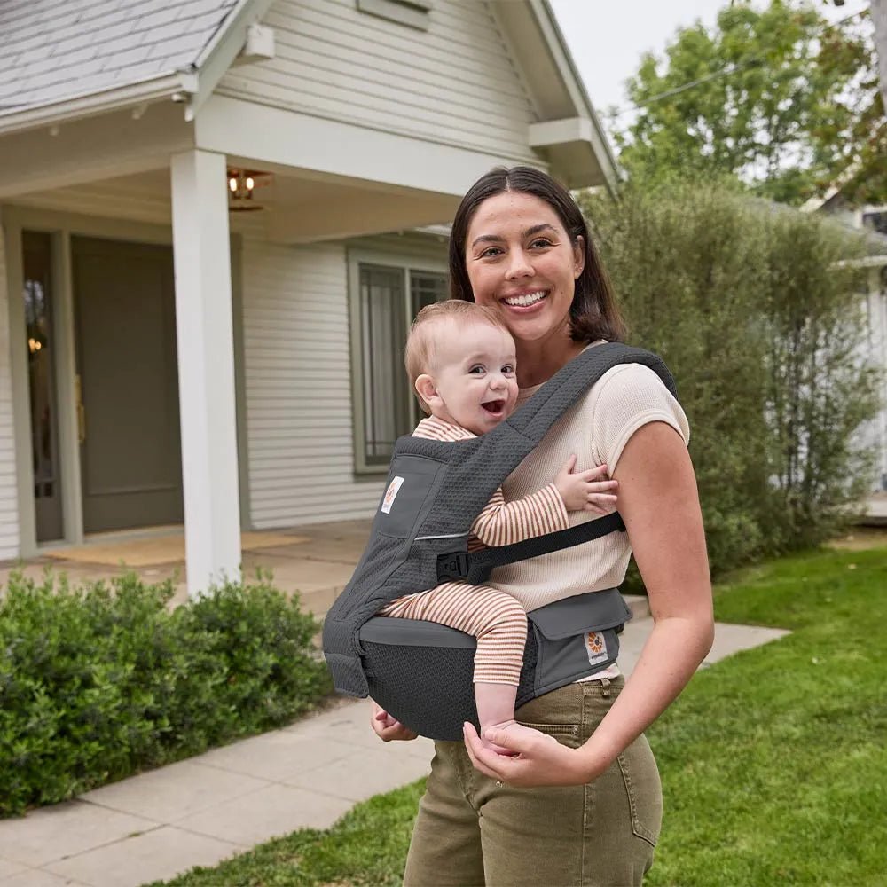 Ergobaby Alta Hip Seat Baby Carrier in gray, worn by a smiling mom front-carrying her baby for close bonding.