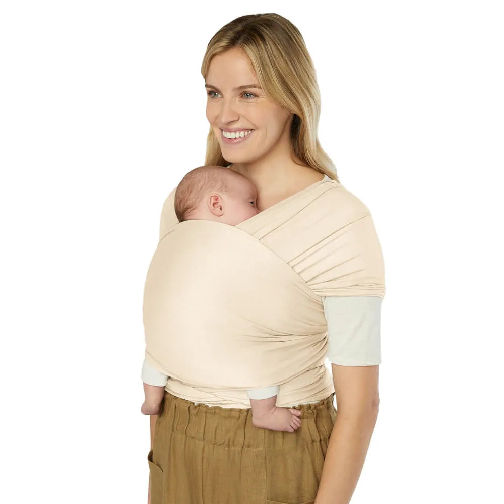 ERGOBABY Aura baby wrap in beige sustainable knit worn as cradle carry for newborn.