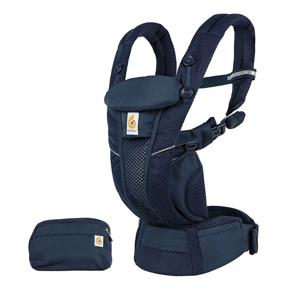 Ergobaby Omni Breeze navy baby carrier worn on wearer, featuring padded mesh straps, waist belt, and matching pouch.