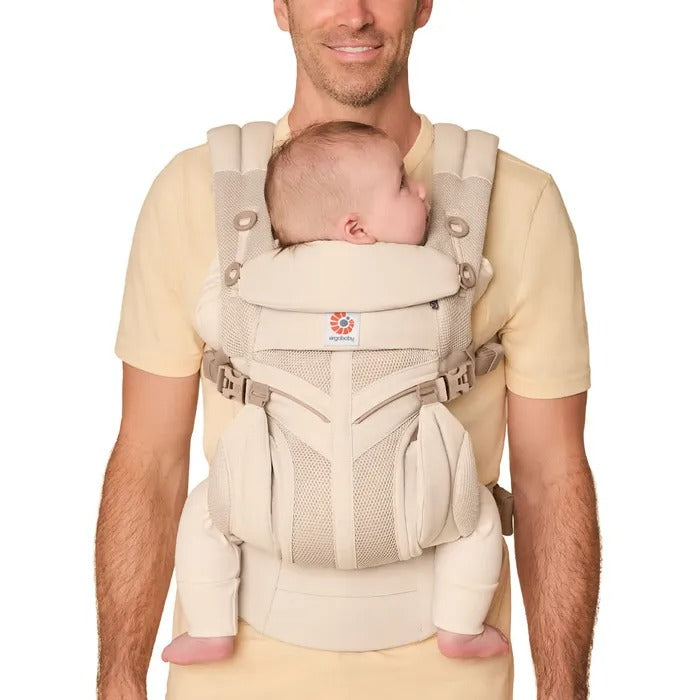 Ergobaby Omni Classic Mesh Baby Carrier Natural Beige worn by dad with baby snug against chest; breathable mesh panels visible.