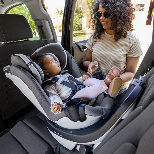 Evenflo Gold Revolve360 Slim 2-in-1 rotational car seat with SensorSafe, gray, installed in car with caregiver