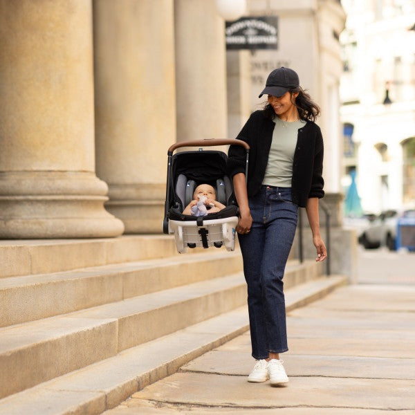 Evenflo Gold Shyft Dualride infant car seat and stroller combo with CarryAll storage; mom walks city sidewalk.