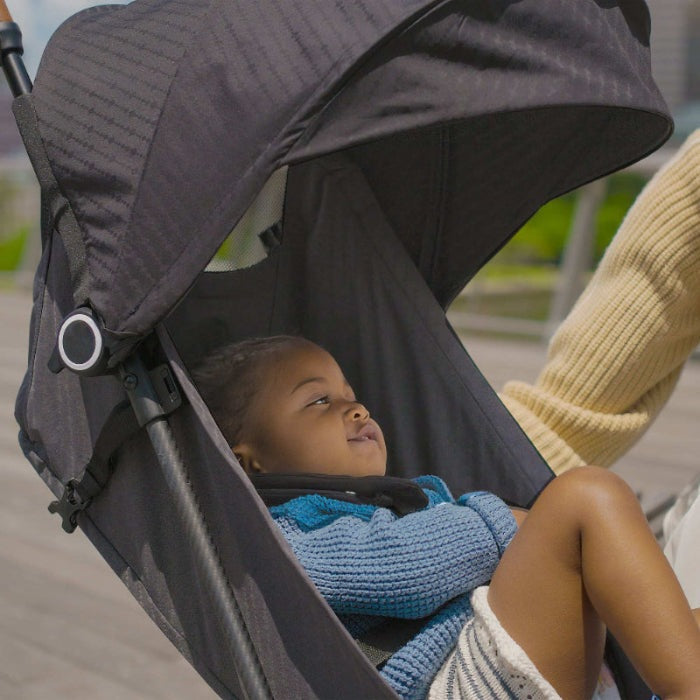 Evenflo Hummingbird ultralight carbon fiber stroller with a baby in a blue knit sweater under a black canopy