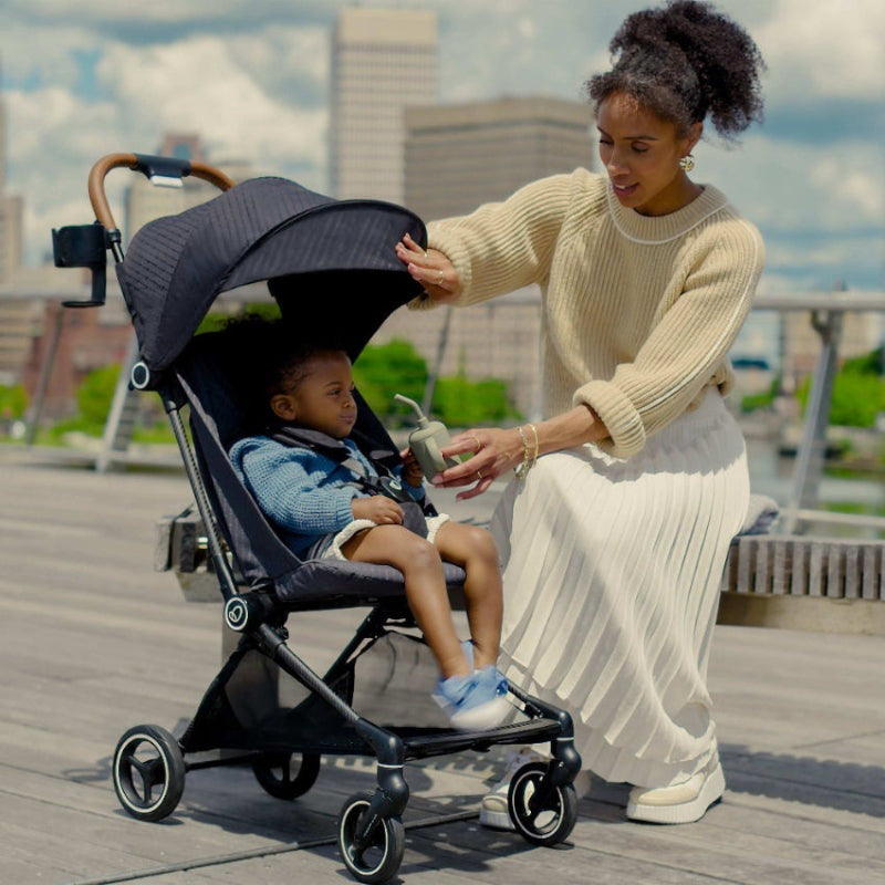 Evenflo Hummingbird Ultra-Lightweight Carbon Fiber Stroller on a boardwalk with mother and baby under canopy