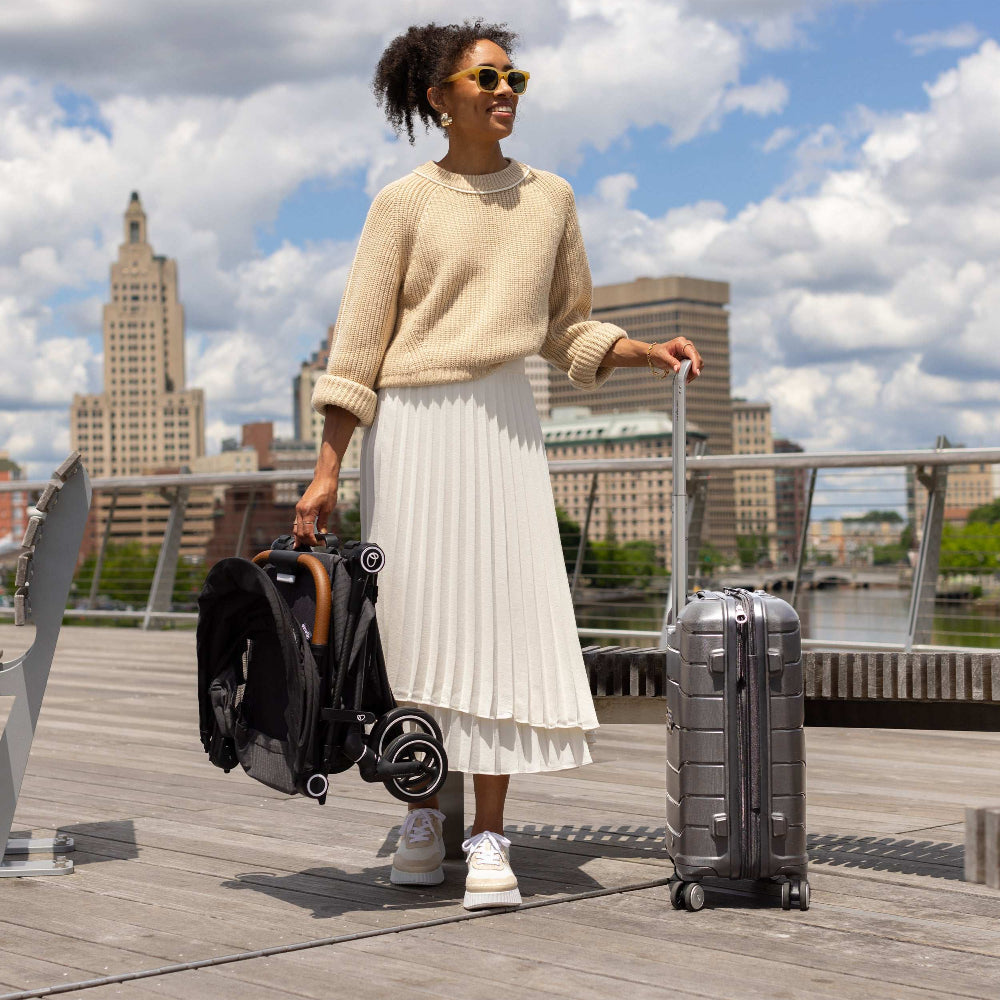 Evenflo Hummingbird Ultra-Lightweight Carbon Fiber stroller and silver rolling suitcase on a boardwalk.