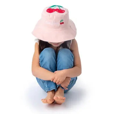 Flapjackkids Reversible Kids Sun Hat, pink with cat and cherry print, worn by a seated child.