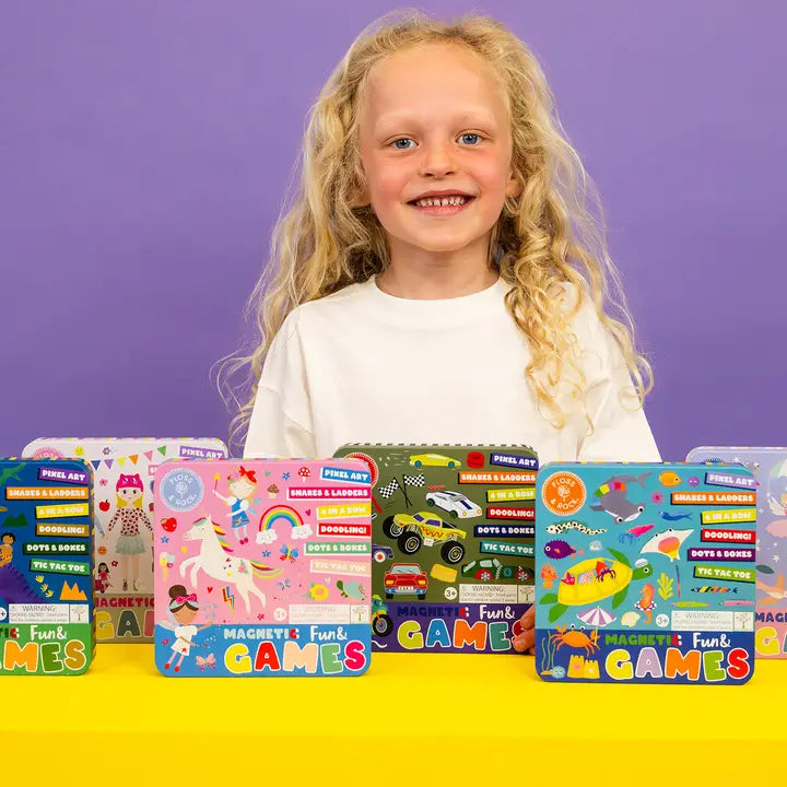 Floss and Rock Magnetic Fun & Games Tin set of five on a yellow table, girl smiling behind them.