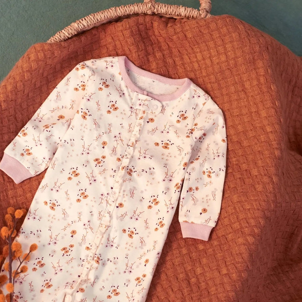 Gerber Baby Boys Floral Sleep 'N Play laid flat on a warm orange blanket, white with peach flowers and pink trim.