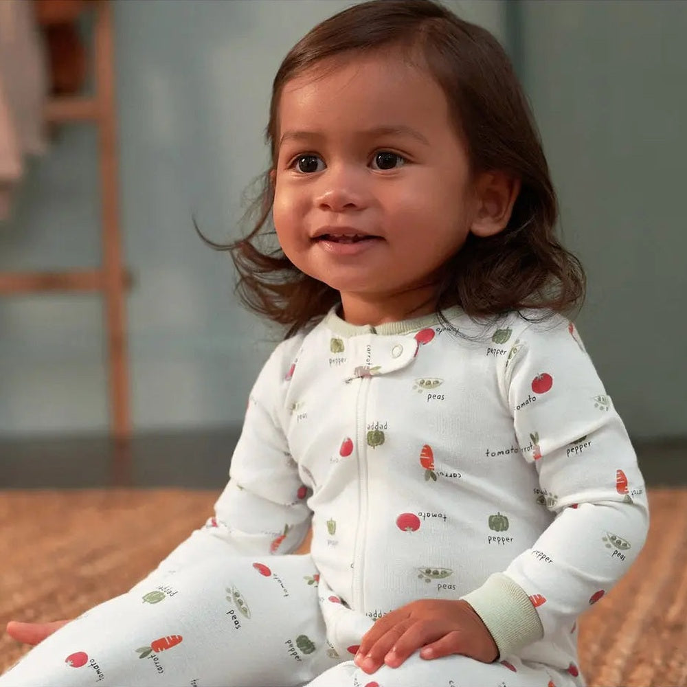 Gerber Baby Neutral Veggies Sleep N Play in pale blue with veggie prints; toddler sits upright on a rug.