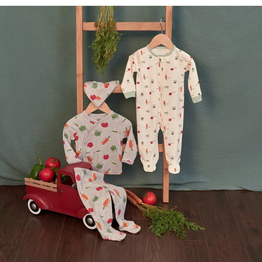 Gerber Baby Neutral Veggies Sleep N Play in white cotton with veggie print, displayed on hangers beside a red toy truck.