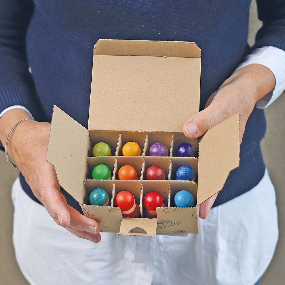 Grimm's 12 Rainbow Friends wooden beads set in a divided cardboard box with vibrant rainbow colors