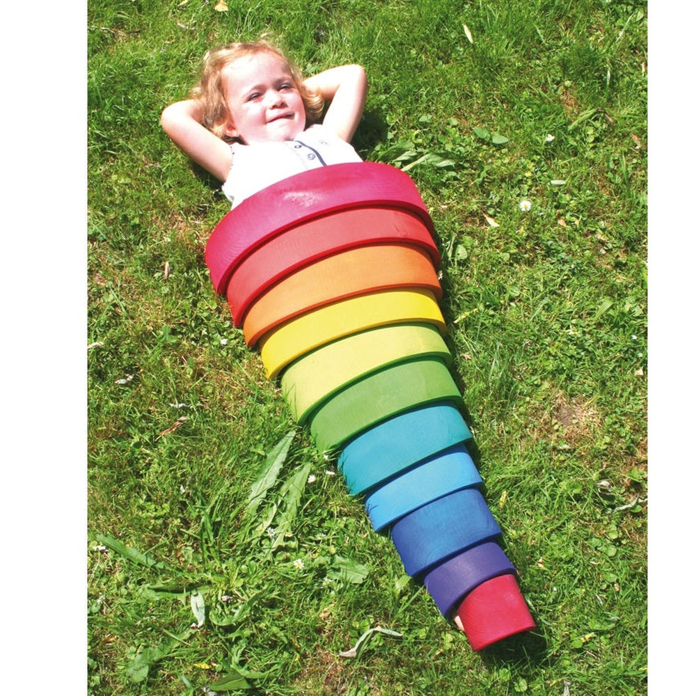Grimm's Building Rainbow Large 12pc wooden rainbow stack on grass with a child playing